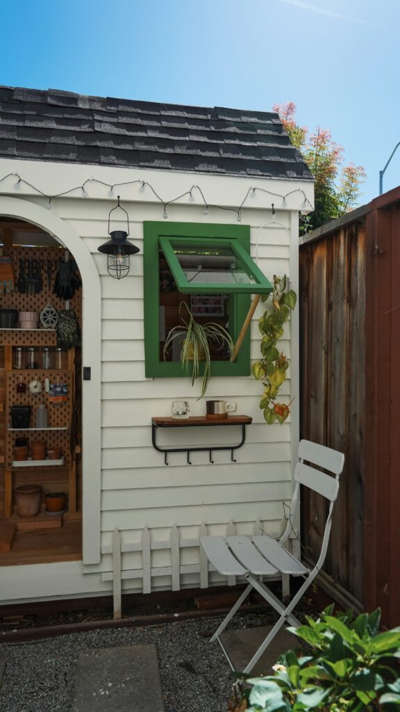 A small white garden shed with a green window